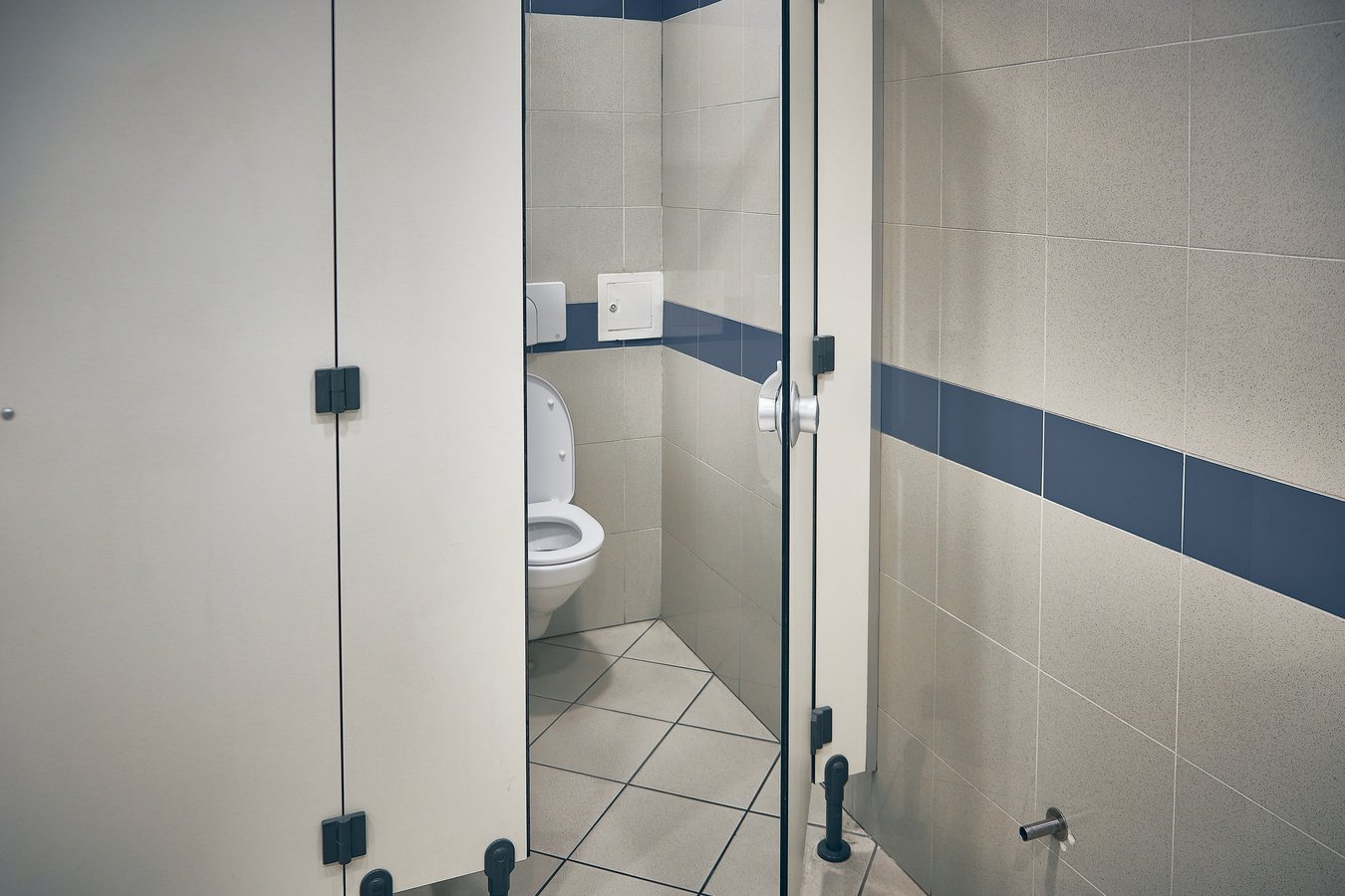 Open door of public toilet stall. Toilet bowl inside toilet stall